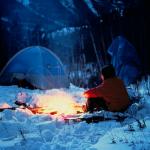 winter camping at night man sitting by fire near tent
